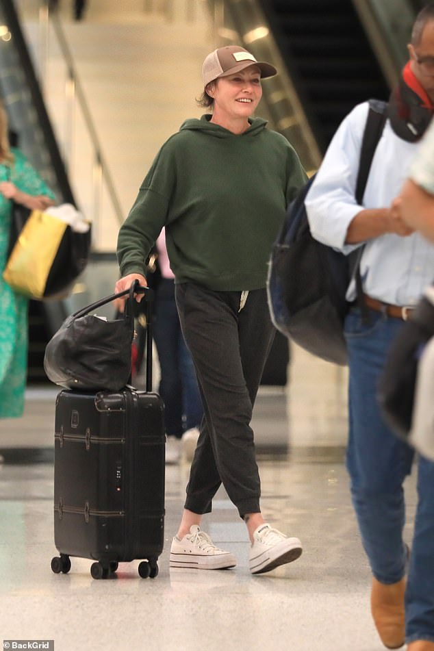 Комфортно: 52-летняя выпускница Беверли-Хиллз 90210 улыбалась и выглядела счастливой, катя свой багаж через оживленный терминал.