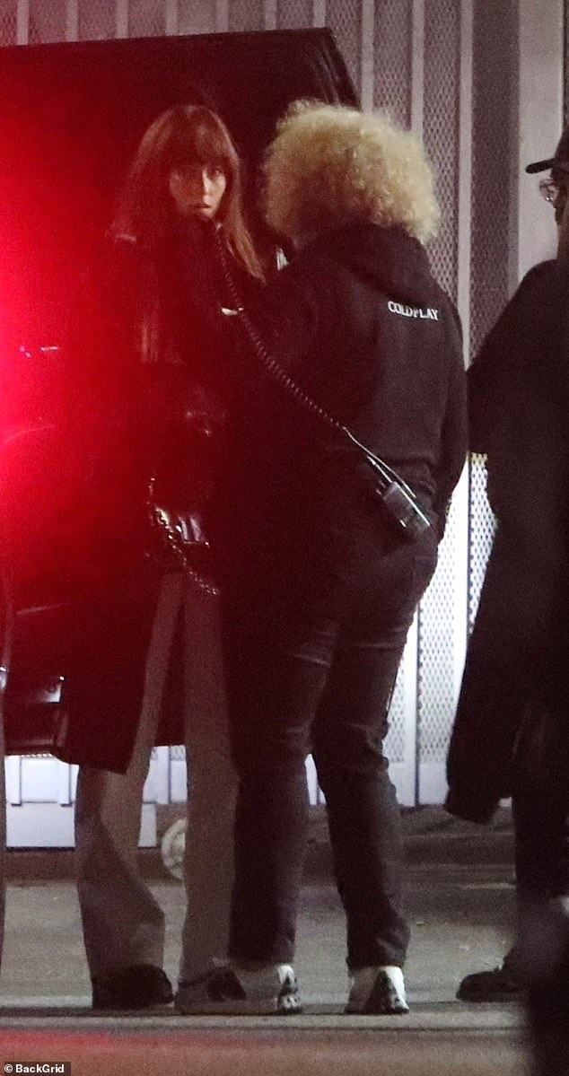 Актриса, которая играет Анастейшу Стил в фильмах «Пятьдесят оттенков серого», темно-каштановые локоны были распущены и с челкой, она была одета в черное кожаное пальто, светло-серые брюки и черные туфли.