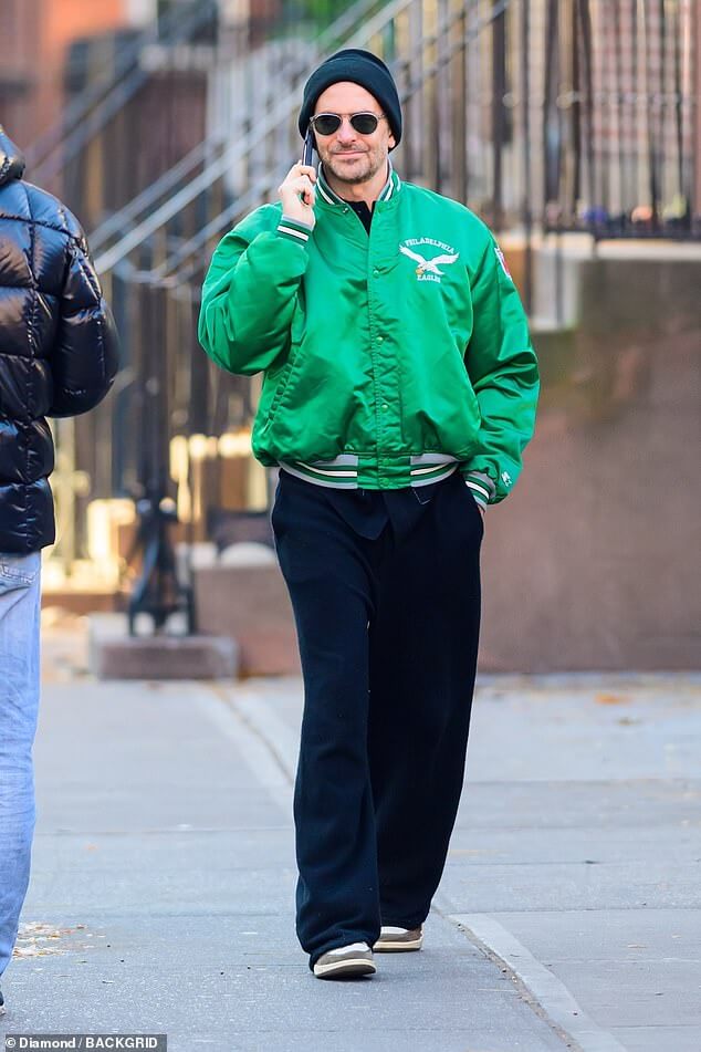 Брэдли Купер выделяется в ярко-зеленой куртке Philadelphia Eagles во время разговора по телефону в Нью-Йорке… после получения награды Gotham Awards.