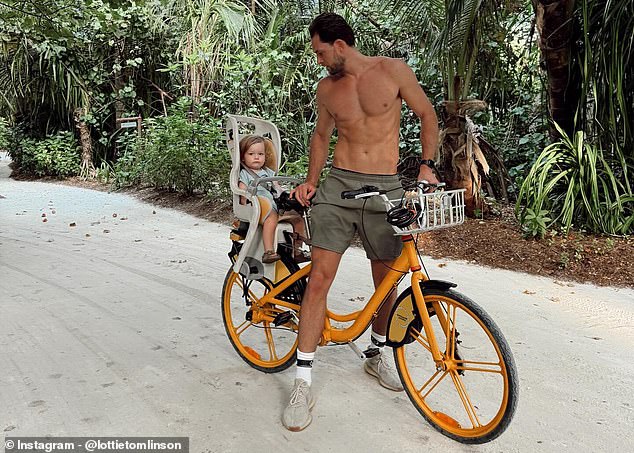 Льюиса сфотографировали катающимся на оранжевом велосипеде без рубашки и напрягающим пресс, когда он повернулся, чтобы проверить Лаки в детском кресле.