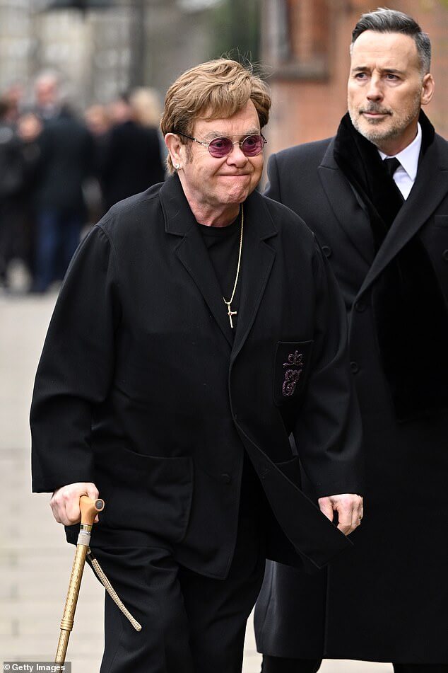 76-летний Элтон Джон демонстрирует травму стопы и ходит с палкой, когда он присоединяется к 61-летнему мужу Дэвиду Фернишу на похоронах Дерека Дрейпера… после трогательных проявлений поддержки скорбящей Кейт Гарравэй