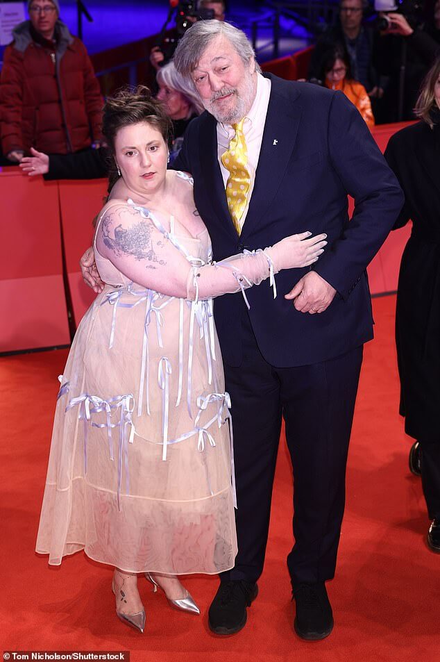 Лена Данэм ошеломляет полупрозрачным платьем с лентой, обнимаясь со Стивеном Фраем на премьере «Другой конец» во время Берлинского кинофестиваля.
