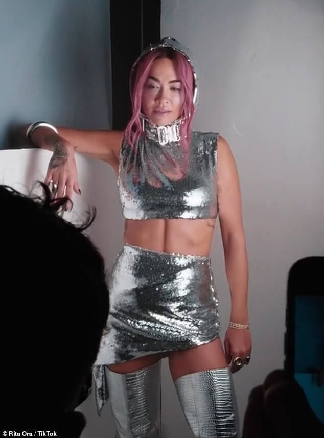 Рита Ора демонстрирует свой подтянутый пресс в комбинезоне с серебряными блестками, демонстрируя свои новые розовые волосы в закулисном видео к новому синглу Last Of Us