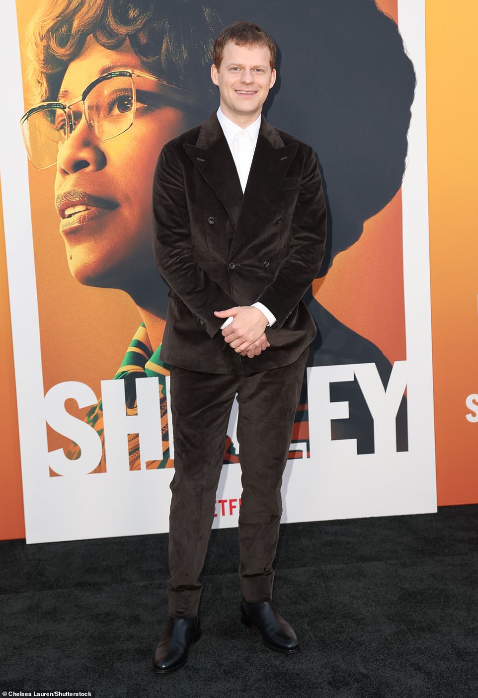 Лукас Хеджес, который играет Роберта Готлиба, демонстрирует шикарную фигуру в коричневом бархатном костюме и белой рубашке на пуговицах.