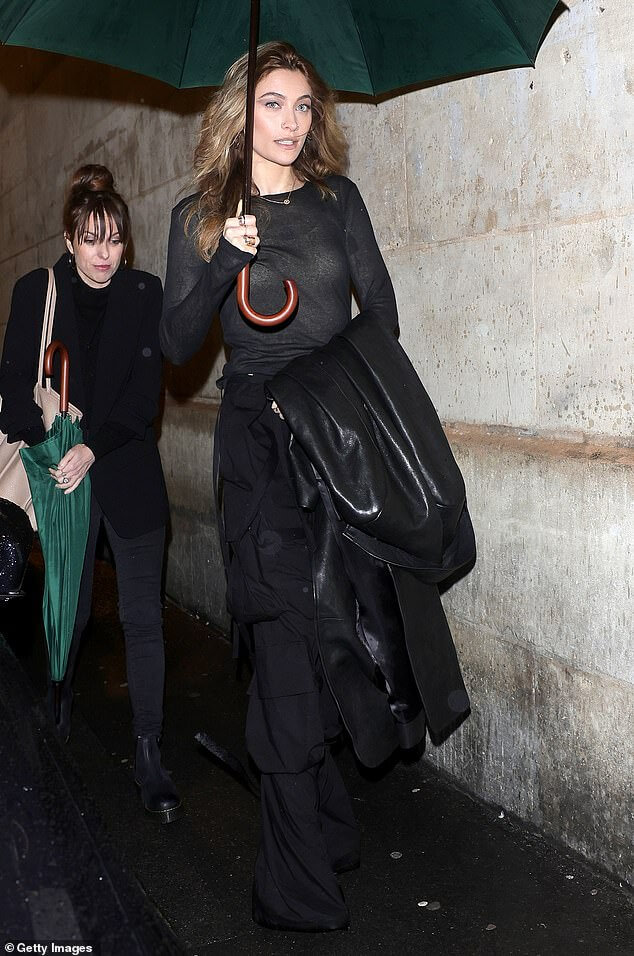 Пэрис Джексон в прозрачной черной рубашке и брюках-карго выдерживает дождь во время Недели моды в Париже.