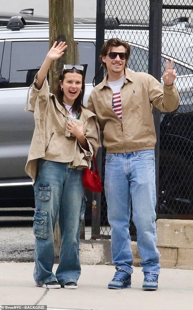 Милли Бобби Браун, 20 лет, и жених Джейк Бонджови, 21 год, одеты в коричневые рубашки и с энтузиазмом машут рукой во время прогулки по Нью-Йорку.