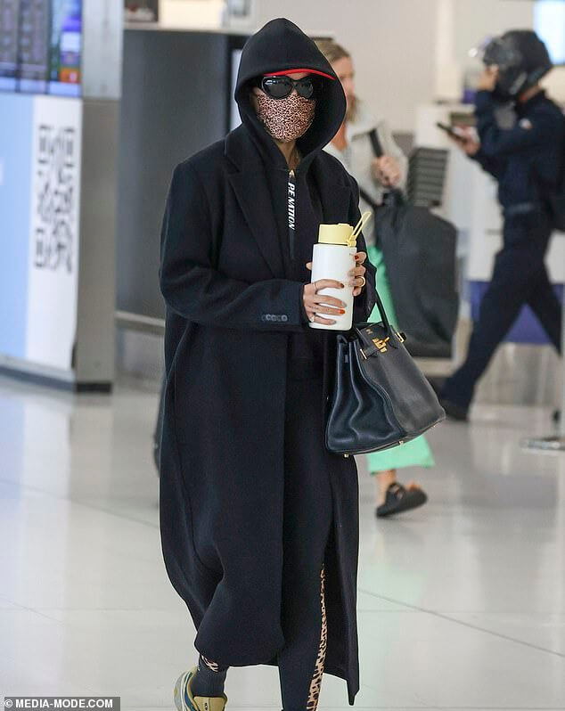 Угадай кто!  Международная поп-звезда остается инкогнито в аэропорту Сиднея, надев длинное пальто, маску и солнцезащитные очки.