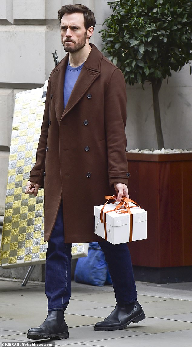 Нахмуренный британец был одет в шоколадно-коричневое двубортное пальто, такое же, как то, которое он носил в конце марта, и держал в руках белую подарочную коробку.