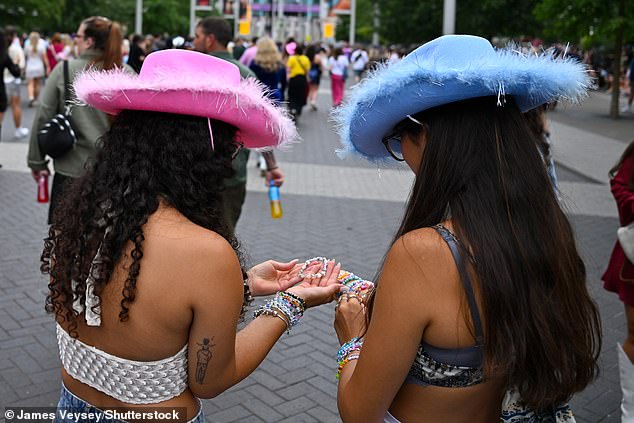Пара Swifties в розовых и синих ковбойских шляпах смотрят на браслеты в ожидании начала концерта.